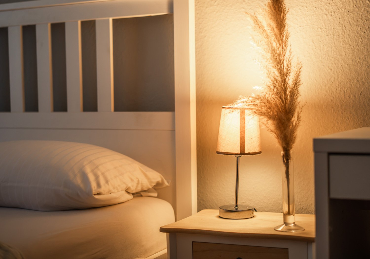 Hotelbett mit Nachttischlampe und Trockenblumen