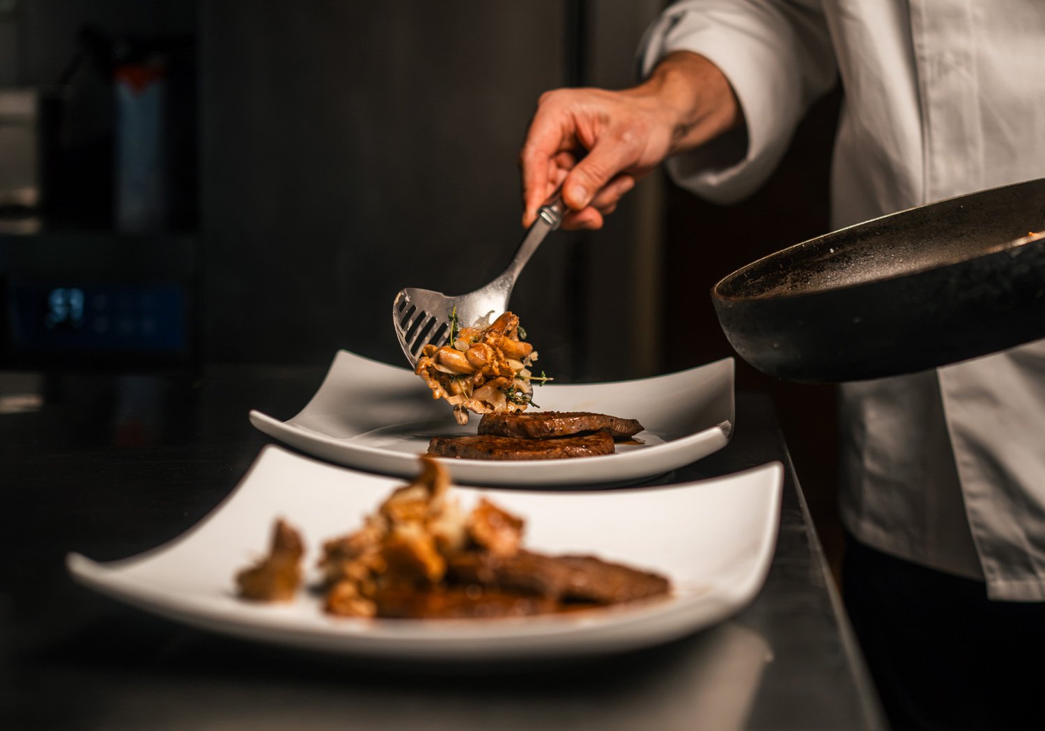 Anrichten von Fleisch und Pilzen auf weißen Tellern